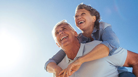 Man giving his partner a piggy back with blue sky and sun above