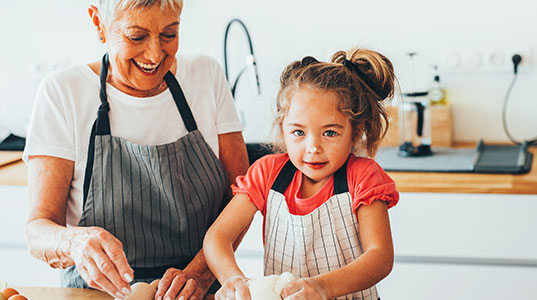 Grandmother helping her granddaughter bake in the kitchen, both wearing aprons