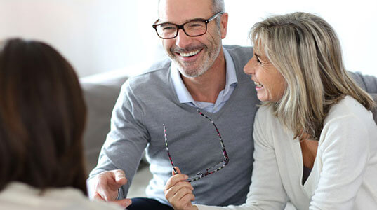 A couple smiling, and talking to a third person inside